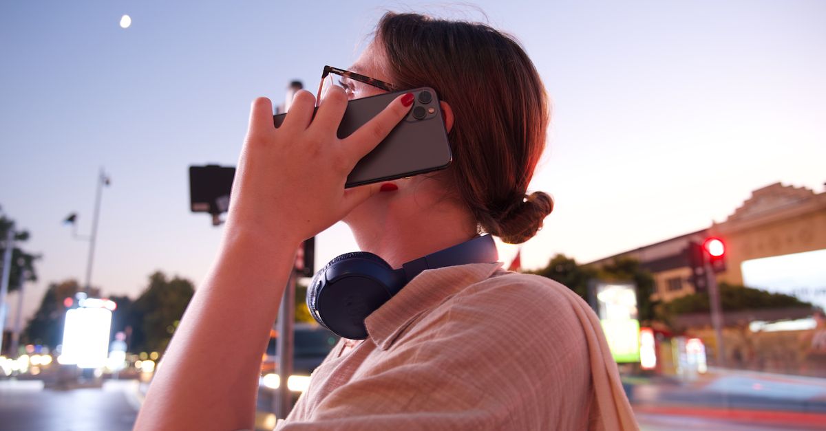 Woman talking on smartphone at dusk, urban setting with blurred city lights and headphones. Ideal for lifestyle or technology themes.